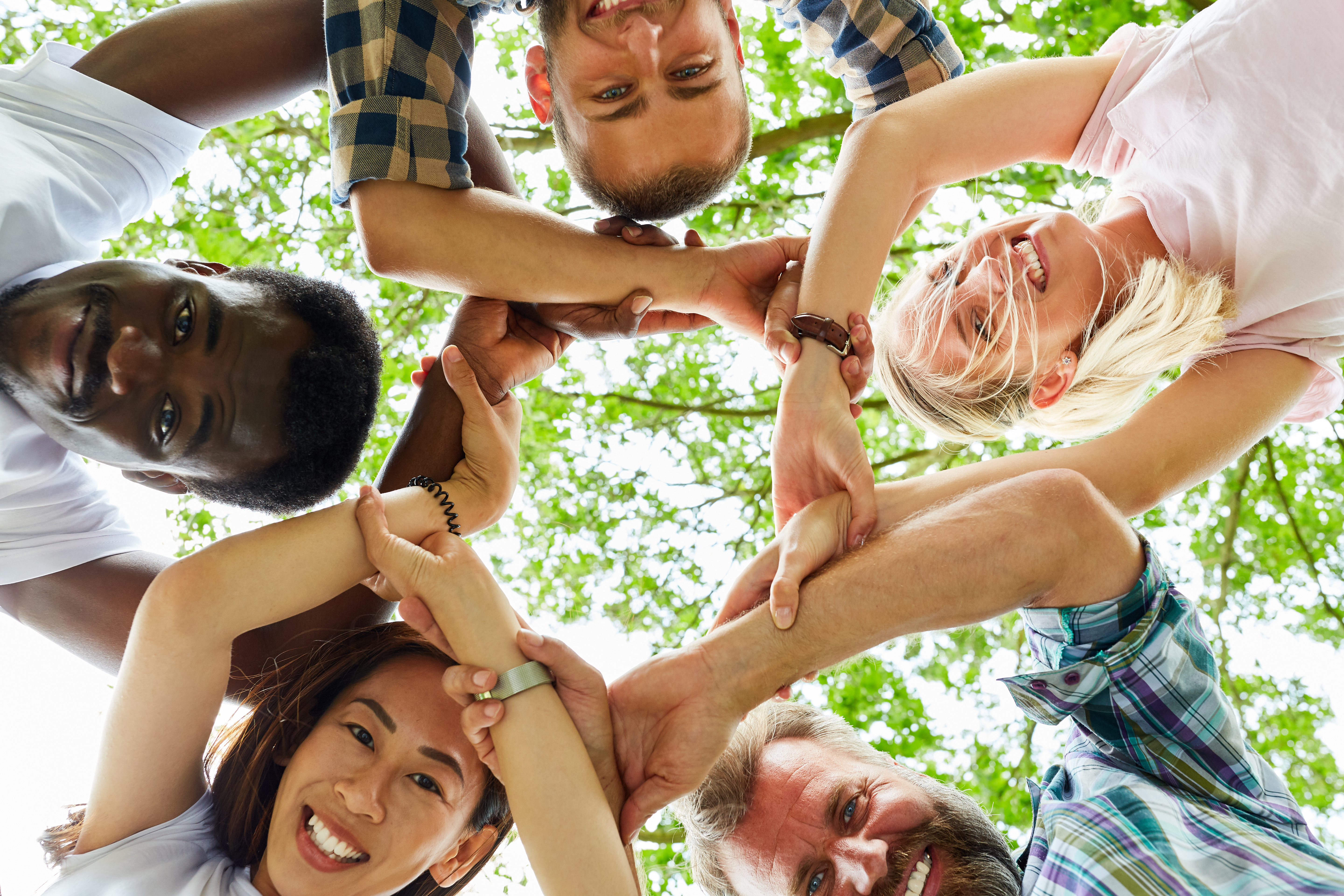Eine Gruppe von Menschen unterschiedlichen Geschlechts und Herkunft bildet einen Kreis mit Händen