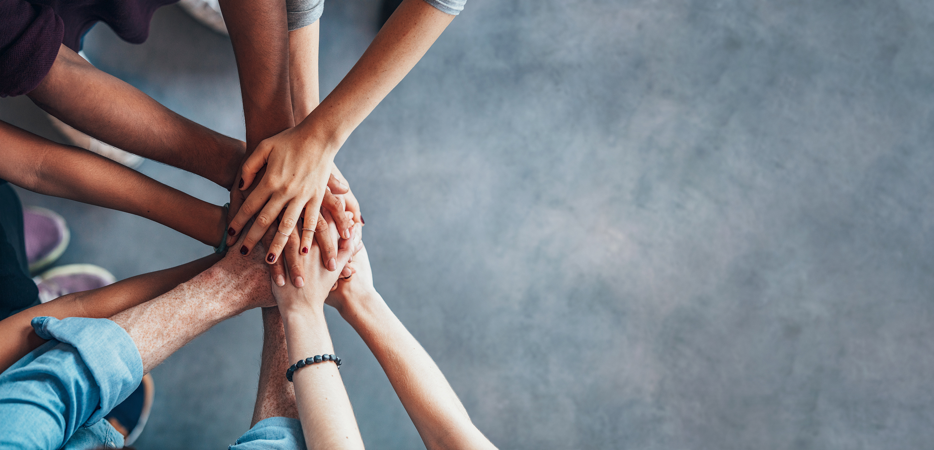 Vogelperspektive auf eine Gruppe von aufeinandergelegten Händen unterschiedlicher Menschen