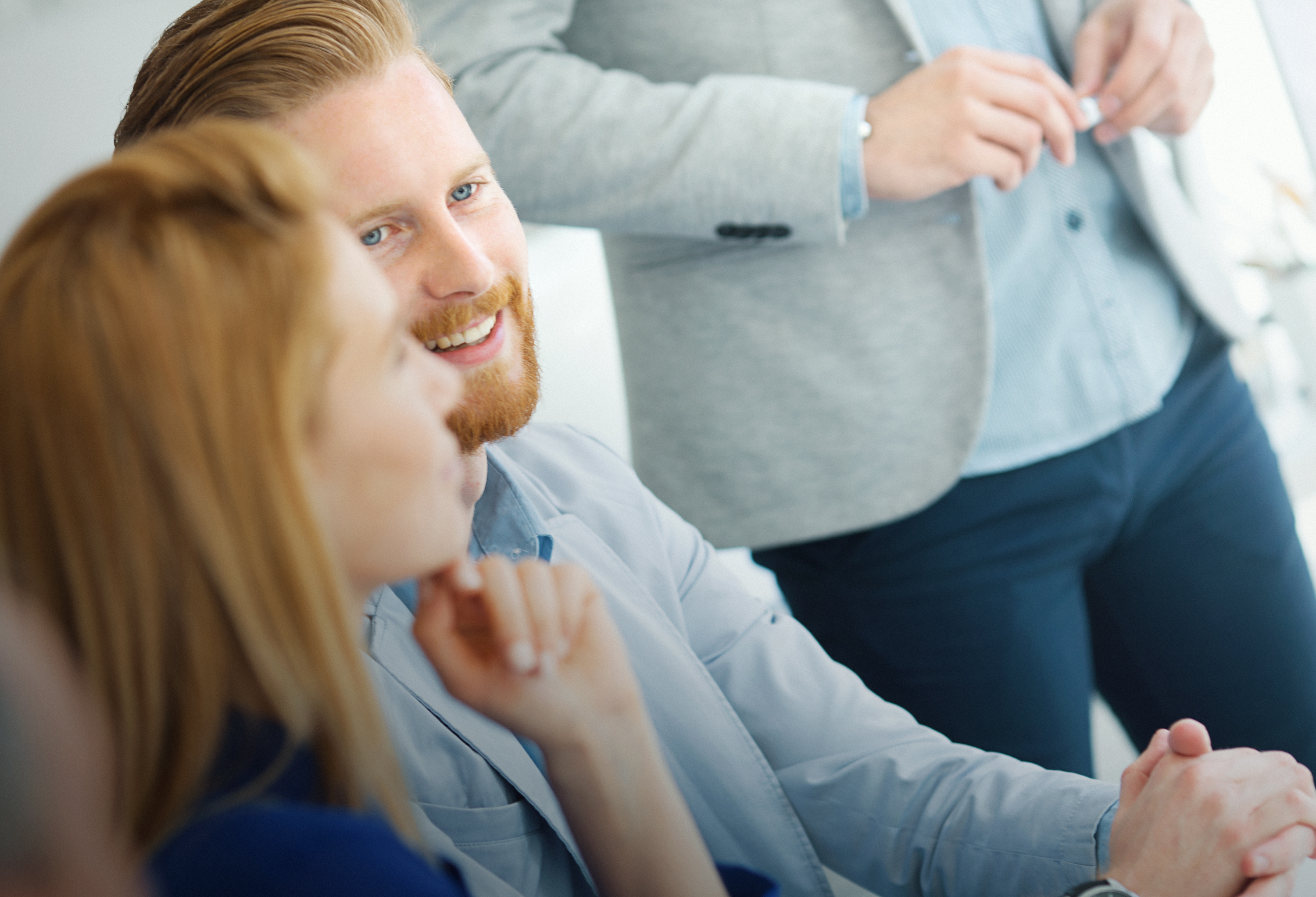 Drei Menschen in Business-Kleidung sitzen in einem Büro und unterhalten sich gut gelaunt